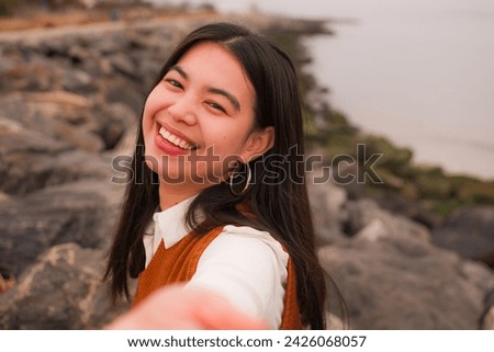 Selfie of a Cute asian young lady, she is smiling and having fun, shore and ocean background