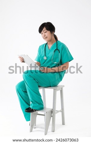 Female Asian doctor wearing a green scrubs reading a chart. Isolated on white.