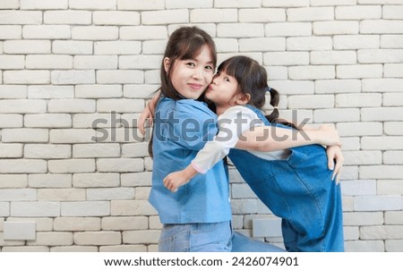 Happy asian beautiful young mother and cute daughter little girl smiling  posing kissing on white brick wall background studio portrait Mother's Day love family parenthood childhood concept.
