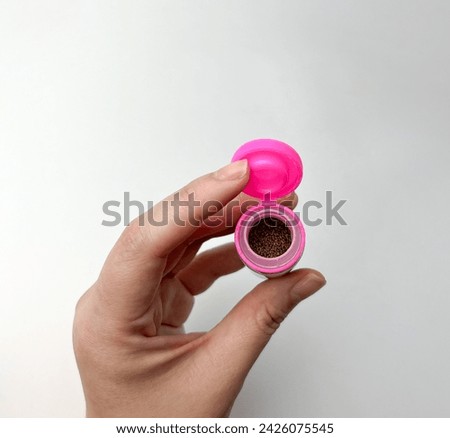 Hand holding small micro natural pet fish food inside plastic bottle packaging with opened pink colored lid. Object photography isolated on white background.