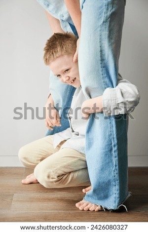 Young happy boy hugging mom's legs. Hyperactive kid holding his mother's legs. Clingy son wanting attention from mommy. Royalty-Free Stock Photo #2426080327