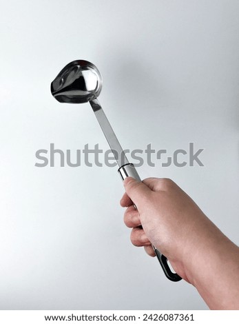 Hand holding stainless metal soup spoon ladle with pouring hole. cooking kitchen utensil tools isolated object photography on white studio background.