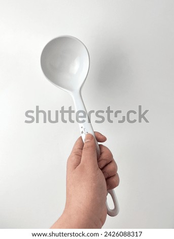 Hand holding white plastic soup ladle spoon. Cooking kitchen utensil tools isolated object photography on white studio background.