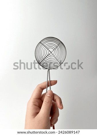 Hand holding small round spiral strainer. Cooking kitchen utensil tools isolated object photography on white studio background.