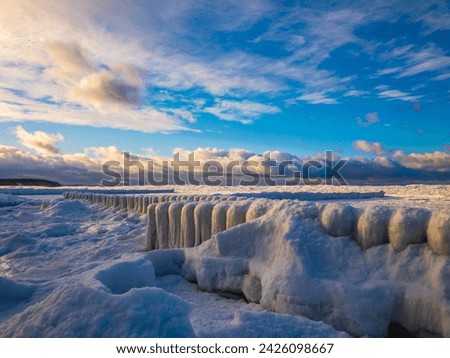 Icy pier extending over a frozen lake with fresh snow, against a backdrop of blue skies and clouds. Royalty-Free Stock Photo #2426098667