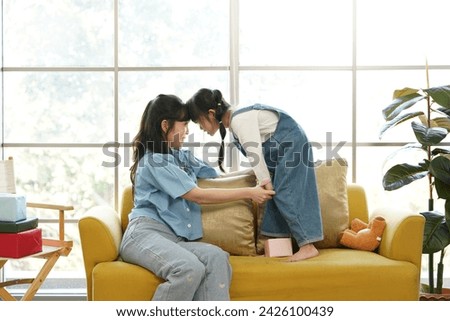 single Asian mother sits on the sofa with her five-year-old daughter, playing with her mother, butting her head in the living room at home.