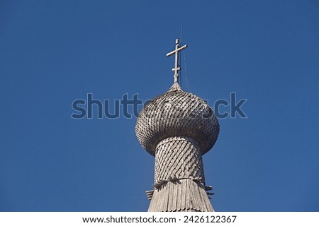 Old wooden church with domes of shingle and a cross against the blue sky, close-up. Traditional orthodox architecture of the north of Russia
