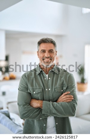 Happy confident middle aged senior man standing with arms crossed at home. Smiling older mature 50 years old handsome man looking at camera posing in modern house living room. Vertical portrait. Royalty-Free Stock Photo #2426125817