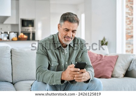 Middle aged old man using smartphone relaxing on couch at home. Happy senior mature male user holding cellphone browsing internet, texting messages on mobile cell phone technology sitting on sofa. Royalty-Free Stock Photo #2426125819