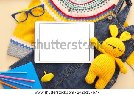 Modern tablet, clothes, stationery and toy bunny on beige background, flat lay. Space for text