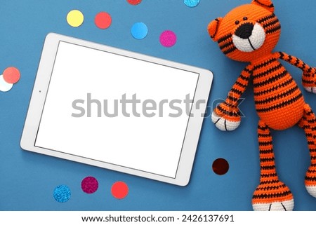 Modern tablet, confetti and toy tiger on blue background, flat lay. Space for text