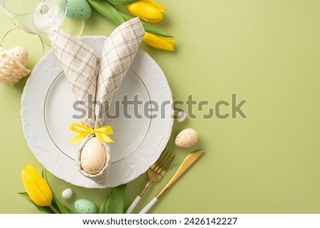 Spring Celebration Table: Overhead shot of an Easter-themed setup—plate, bunny ear napkin, cutlery, wine glass, tulips, and vibrant eggs on a pastel green backdrop. Ideal for festive messages Royalty-Free Stock Photo #2426142227