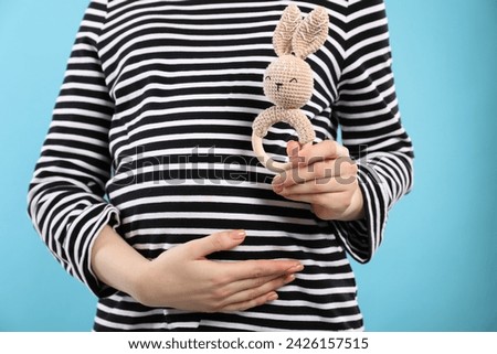 Pregnant woman with baby toy on light blue background, closeup