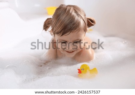 Smiling girl bathing with toy duck in tub