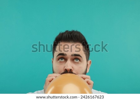 Man inflating bright balloon on turquoise background