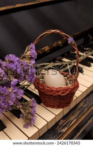 Easter composition with a small basket with one egg on an old piano decorated with purple statice flowers