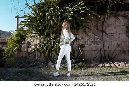Fashion Photography: Woman standing in a rustic house, next to green cactus area, posing for the camera. E-commerce photoshoot. Wearring white outfit. Lifestyle e-commerce