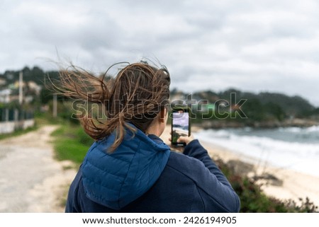 Woman taking a photo with her smartphone at the beach on a cloudy day