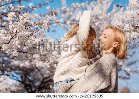 Mother and daughter are happy together in blooming trees garden at spring in sunlight. Woman mom and girl playing, dancing and hugging outdoors. Happy mother's day! Family holiday and togetherness. Royalty-Free Stock Photo #2426195305