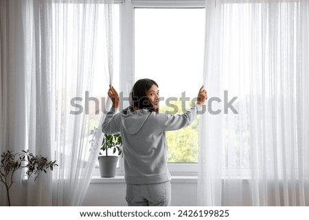Beautiful young Asian woman in stylish hoodie near window at home