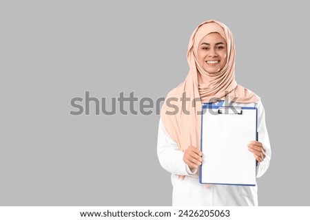 Female Muslim medical intern with clipboard on light background