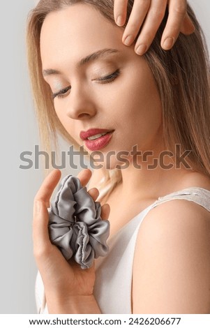 Young blonde woman with scrunchy on light background, closeup