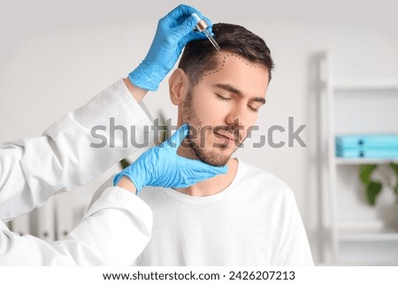 Young man with marked forehead receiving serum for hair growth at hospital, closeup Royalty-Free Stock Photo #2426207213