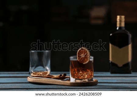 Board with glass of delicious Old Fashioned Cocktail, cinnamon sticks and orange slices on blue wooden table Royalty-Free Stock Photo #2426208509