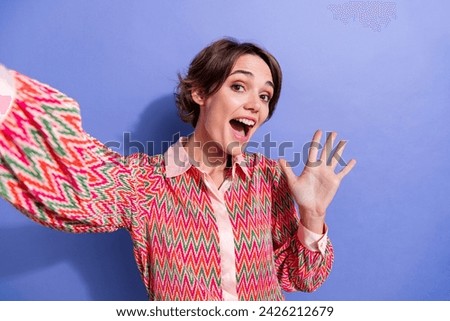 Portrait of cheerful lovely girl with short hair wear stylish shirt doing selfie waving palm say hello isolated on blue color background