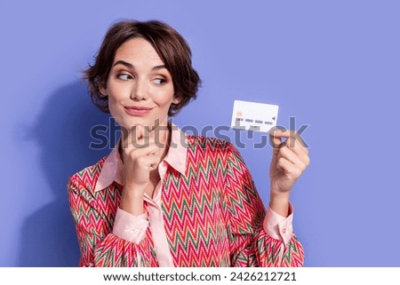 Photo of minded smart positive woman with bob hairstyle dressed print shirt looking at debit card in arm isolated on blue color background