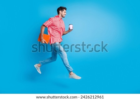 Full size photo of clever man dressed striped shirt run look empty space hold laptop cup of coffee isolated on blue color background