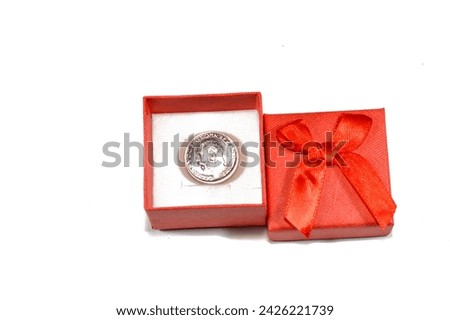 A red gift box with The sovereign, a British silver coin shape, a bullion coin and is sometimes mounted in Jewellery with the design of George and the Dragon on the reverse, pure silver coin