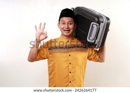 Happy asian muslim man carrying travel suitcase while showing okay hand gesture. Going mudik or travel to hometown for Ramadan eid mubarak celebration