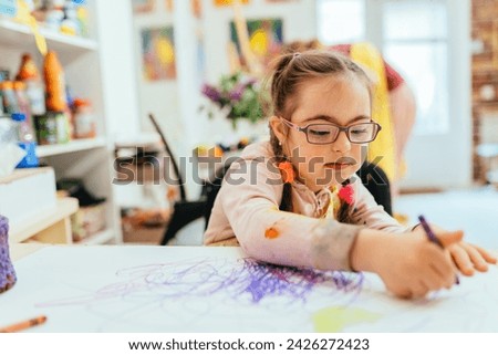 Little girl with special needs in art class painting picture. Happy school kids are doing creative project in classroom.
