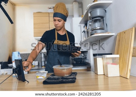young latin man in kitchen at home touching phone screen he paused video tutorial he is watching on internet while preparing cake, he is holding mold to pour mixture. Royalty-Free Stock Photo #2426281205