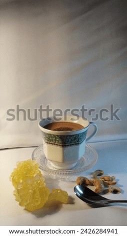 Concept photo of cappuccino coffee served in a glass accompanied by a coffee spoon of rock sugar and cashew nuts beside it with a white background and beautiful lighting