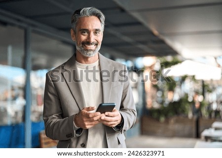 Happy mature older business man executive using mobile cell phone outdoors. Middle aged businessman manager or entrepreneur holding smartphone looking at camera standing outside office. Portrait. Royalty-Free Stock Photo #2426323971