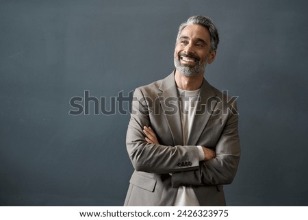 Happy middle aged business man looking away at copy space. Smiling confident 50 years old mature professional businessman executive ceo manager or entrepreneur standing at gray office wall background. Royalty-Free Stock Photo #2426323975
