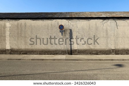 No stopping sign on concrete sidewalk. Grunge concrete building with corrugated sheet metal roof and street in front. Background for copy space.