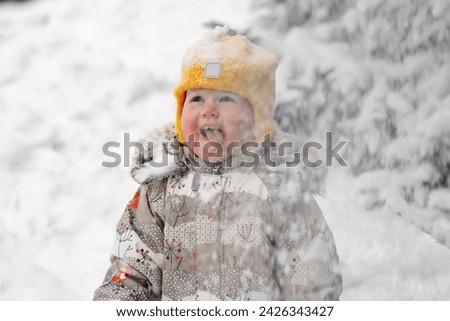 Cute child toddler winces and laughs from snow falling on his face in a winter park