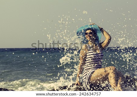 Beautiful woman sitting on a stone and splashing in the sea among the waves