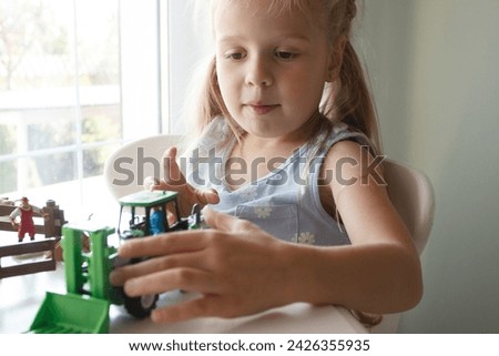 Cute child plays with farm equipment toys. Business or farming concept, blurred background