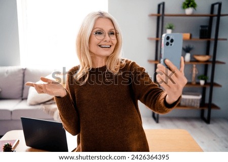 Self portrait of cheerful blonde hair middle age lady in brown pullover has video call demonstrate her living room apartment indoors