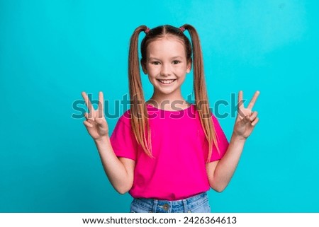 Portrait of adorable positive girl beaming smile demonstrate v-sign isolated on blue color background