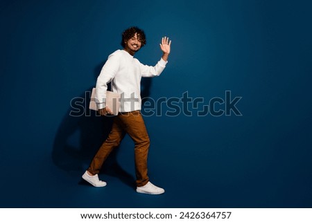Full length photo of good mood funky guy dressed white pullover holding modern device waving hi empty space isolated dark blue color background