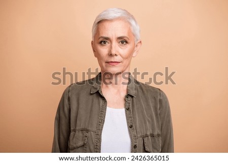 Portrait of middle age blond short hair business lady wearing khaki shirt confident posing non emotional isolated on beige color background Royalty-Free Stock Photo #2426365015