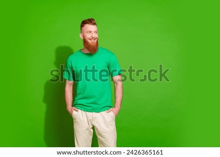 Portrait of good mood cool guy with long red beard wear stylish t-shirt look at promo empty space isolated on green color background