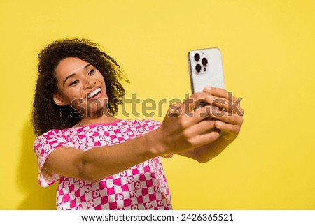 Photo of cute positive girl beaming smile hold smart phone make selfie record video isolated on yellow color background