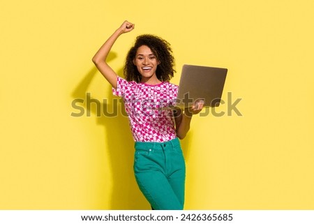 Photo of pretty overjoyed girl hold laptop raise fist triumph accomplishment isolated on yellow color background