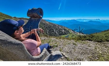 Woman relaxing on wooden chair with view of mountain peaks Karawanks and Julian Alps seen from Goldeck, Latschur group, Gailtal Alps, Carinthia, Austria. Enjoying a break after hiking in Austrian Alps Royalty-Free Stock Photo #2426368473
